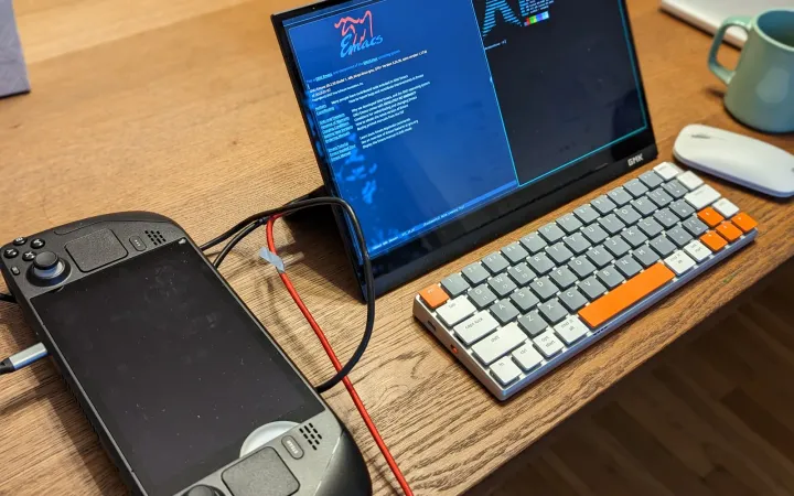 A PC gaming handheld docked to a monitor and keyboard on a desk
