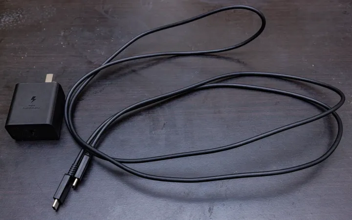 Black Samsung USB-C fast charging adapter and USB-C to USB-C cable on a wooden table
